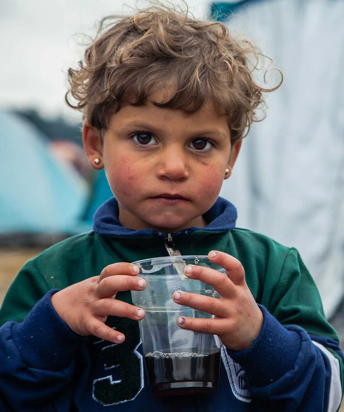  Three year old Lama warms her fingers with a cup of tea. Her family fled their home in Syria but were stranded at the border in Greece for several weeks.