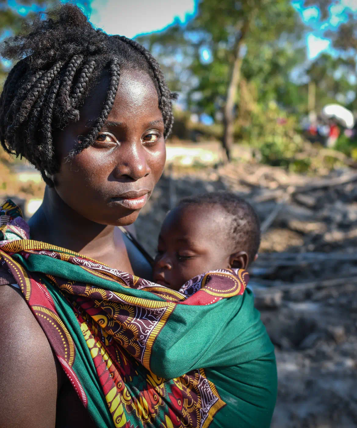 Woman carrying infant in her arms on a devastate field.